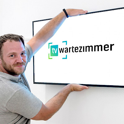 Techniker montiert einen TV-Monitor an die Wand eines Wartezimmers, auf dem das Logo von TV-Wartezimmer zu sehen ist